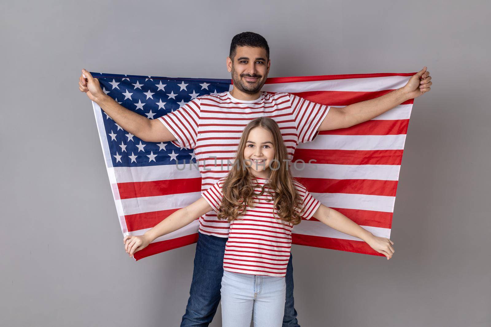Father and daughter in striped T-shirts holding big usa flag, relocation to United States of America by Khosro1