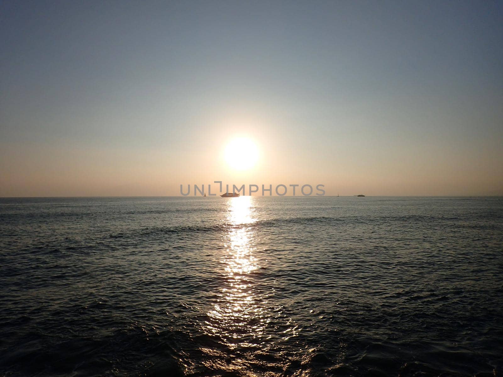 Sunset over the Pacific Ocean with light reflecting on water and boats moving on the horizon off the coast of Oahu, Hawaii.