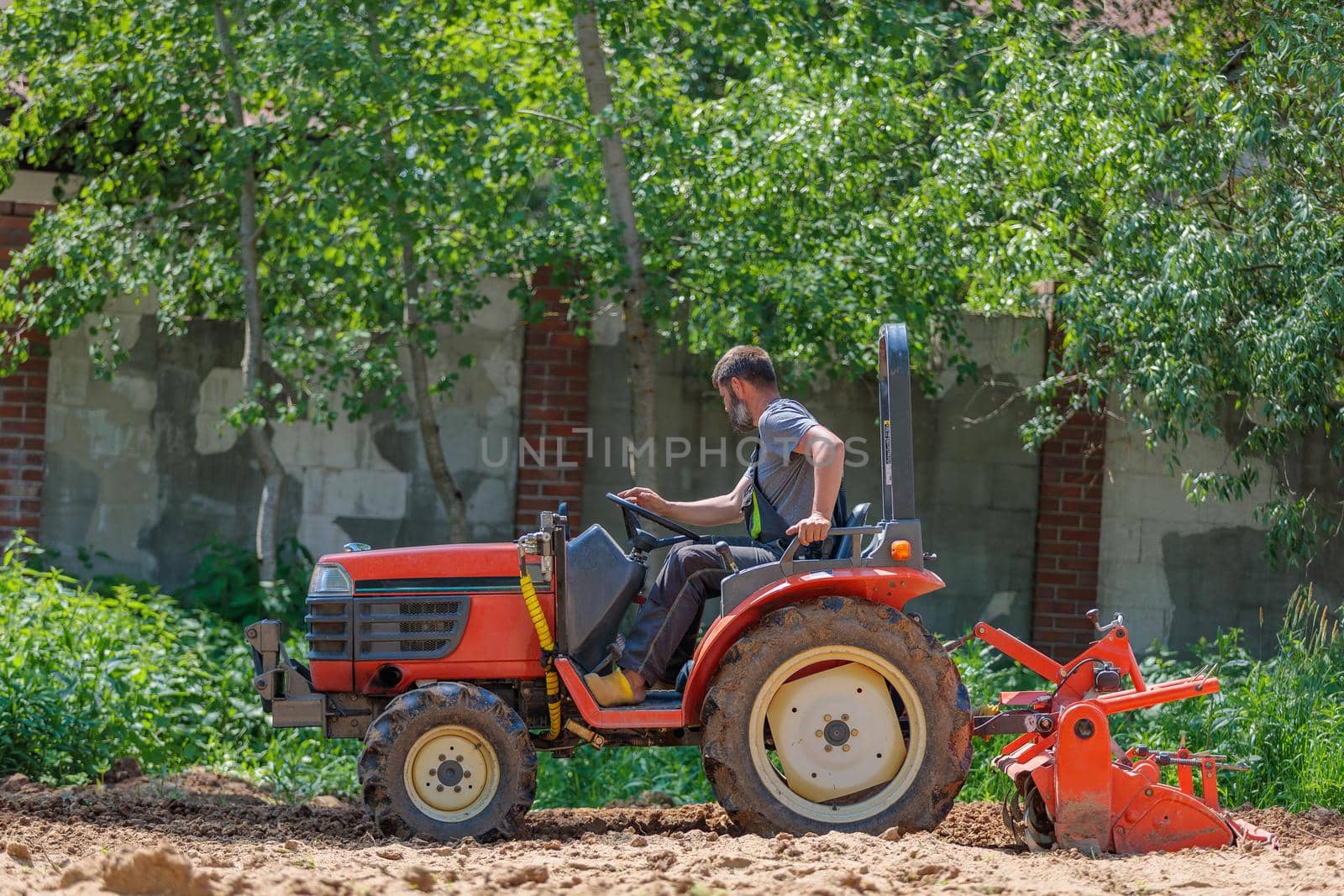 A man on a mini-excavator levels a piece of land, loosens the soil