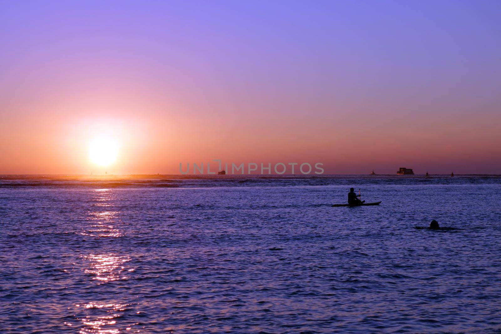 People and boats in the water during Sunset over the ocean at Ala Moana Beach Park on Oahu, Hawaii.