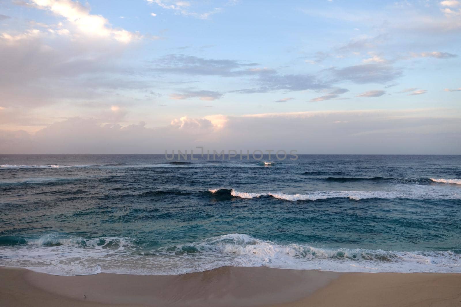 Waves break and crash towards the Hanakailio Beach with dramatic blue cloudy sky on the North Shore of Oahu, Hawaii. 