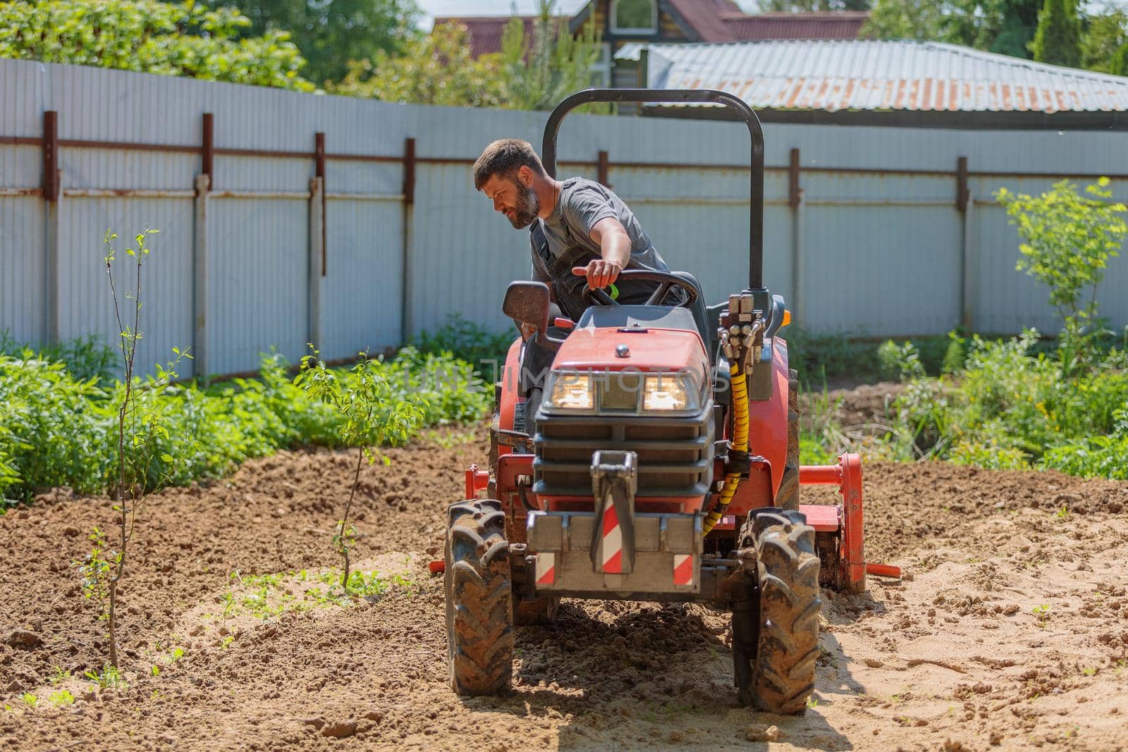 A man on a mini-excavator levels a piece of land, loosens the soil
