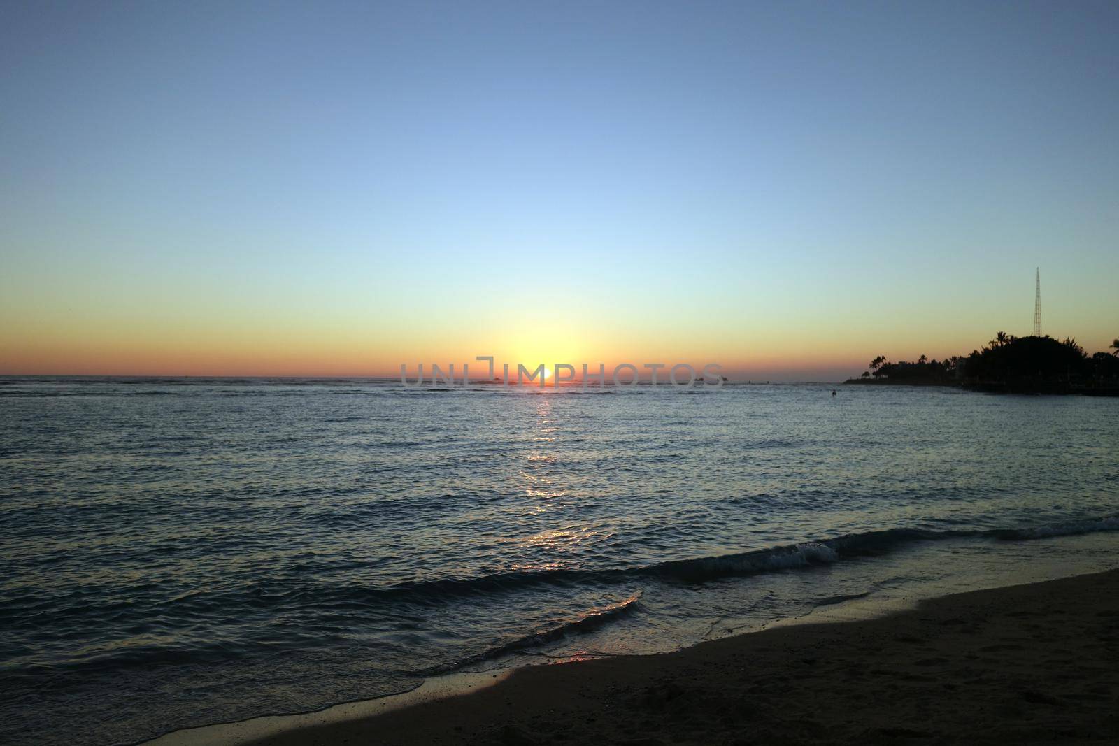 Sunset on as wave lap on the beach from the ocean at Ala Moana Beach Park on Oahu, Hawaii.