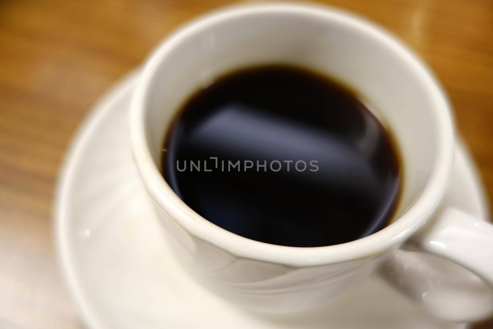 Close-up of Cafe cup of Coffee corner on plate sitting on a wood grain table.