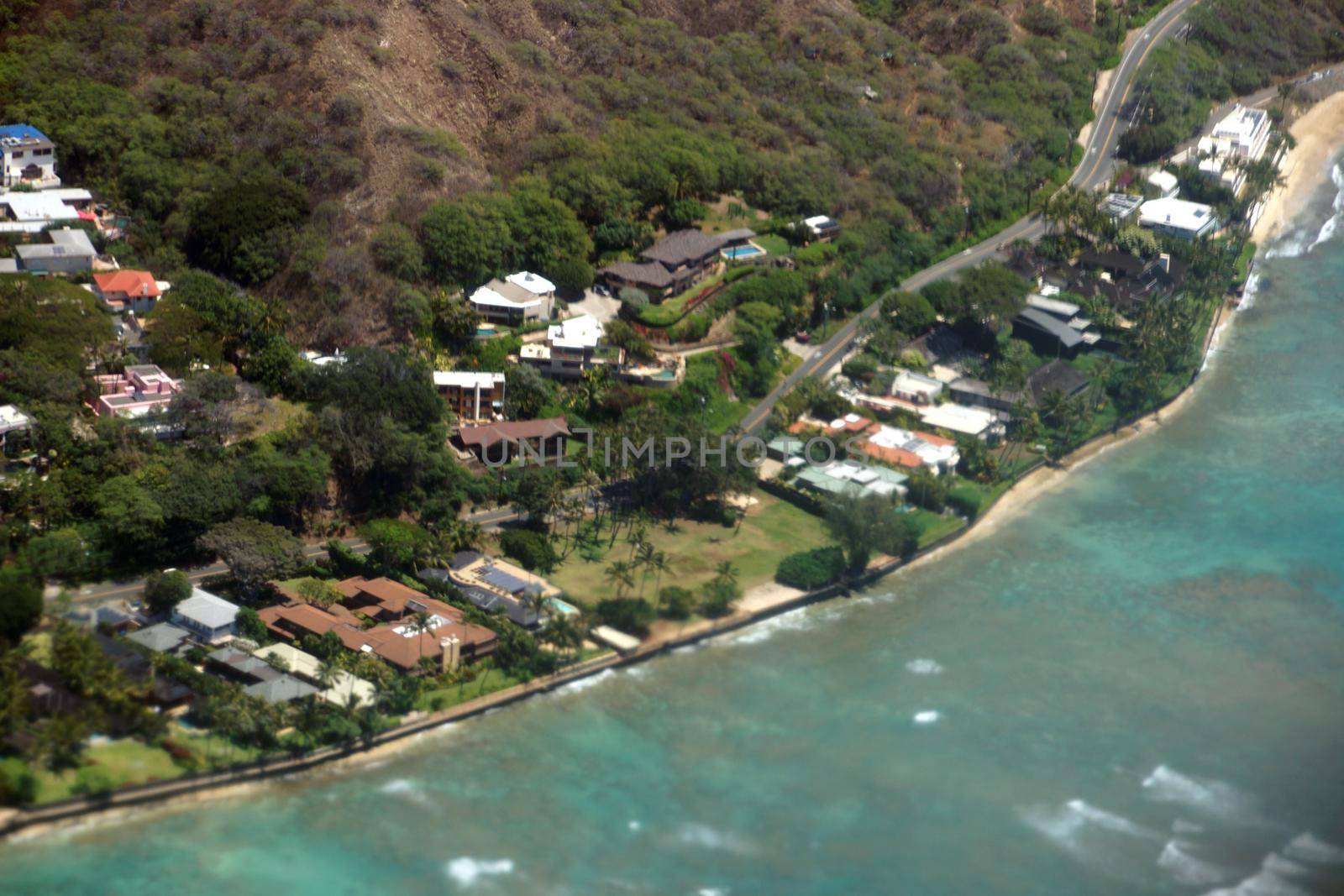 Aerial view of slopes of Diamond Head crater with road surrounded by Luxury homes, Leahi Beach Park, and the shallow ocean waters off shore of the pacific ocean on Oahu, Hawaii on a beautiful day. 