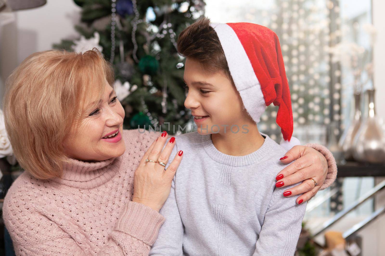 Happy senior woman embracing her young grandson near the Christmas tree at home