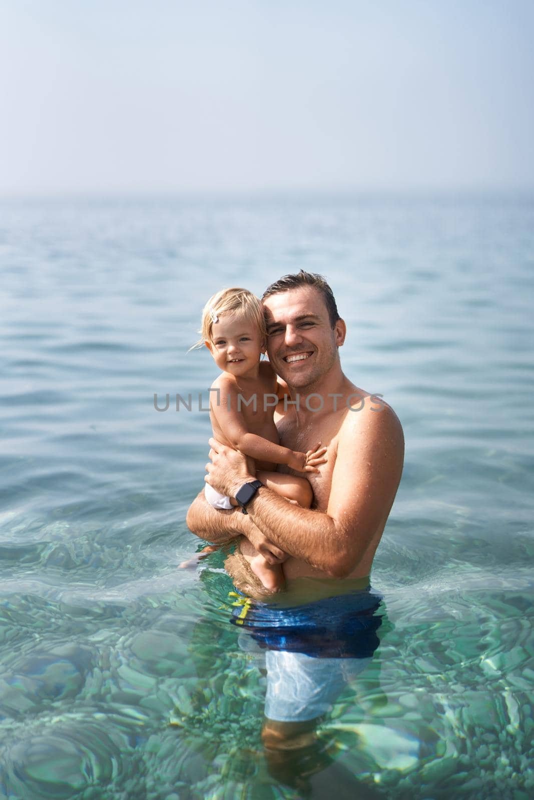 Smiling dad with little girl standing in the sea by Nadtochiy