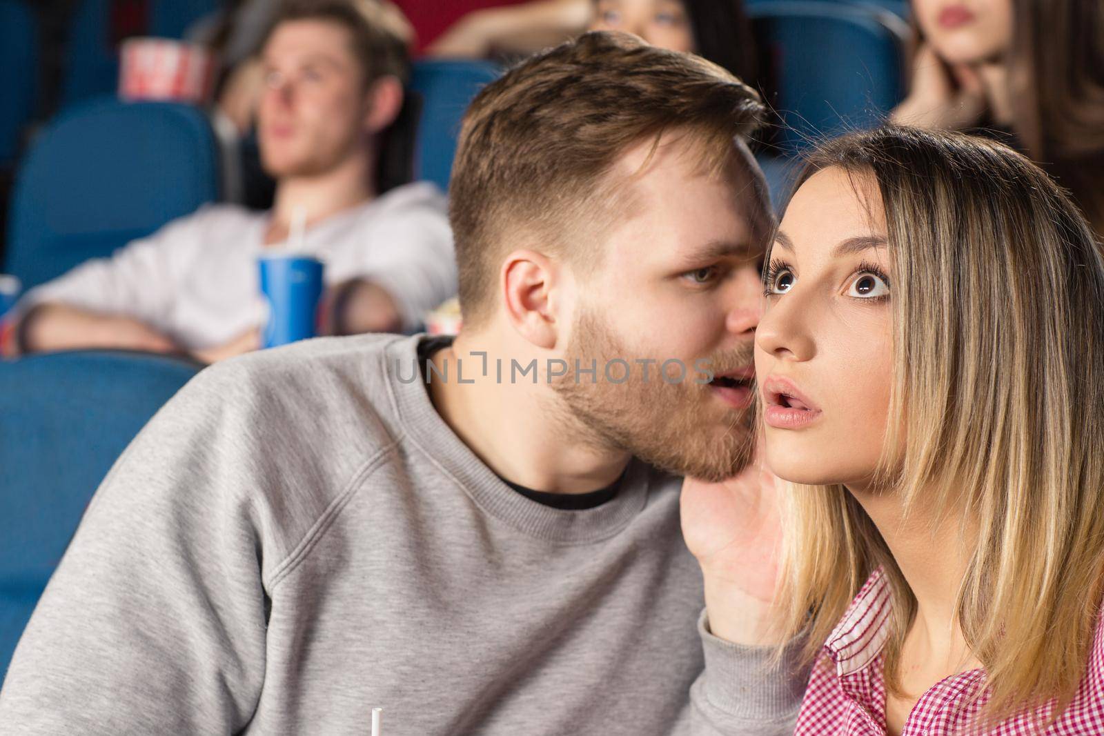 Did you see that? Closeup shot of a young bearded man whispering to his shocked woman at the movies at the local cinema