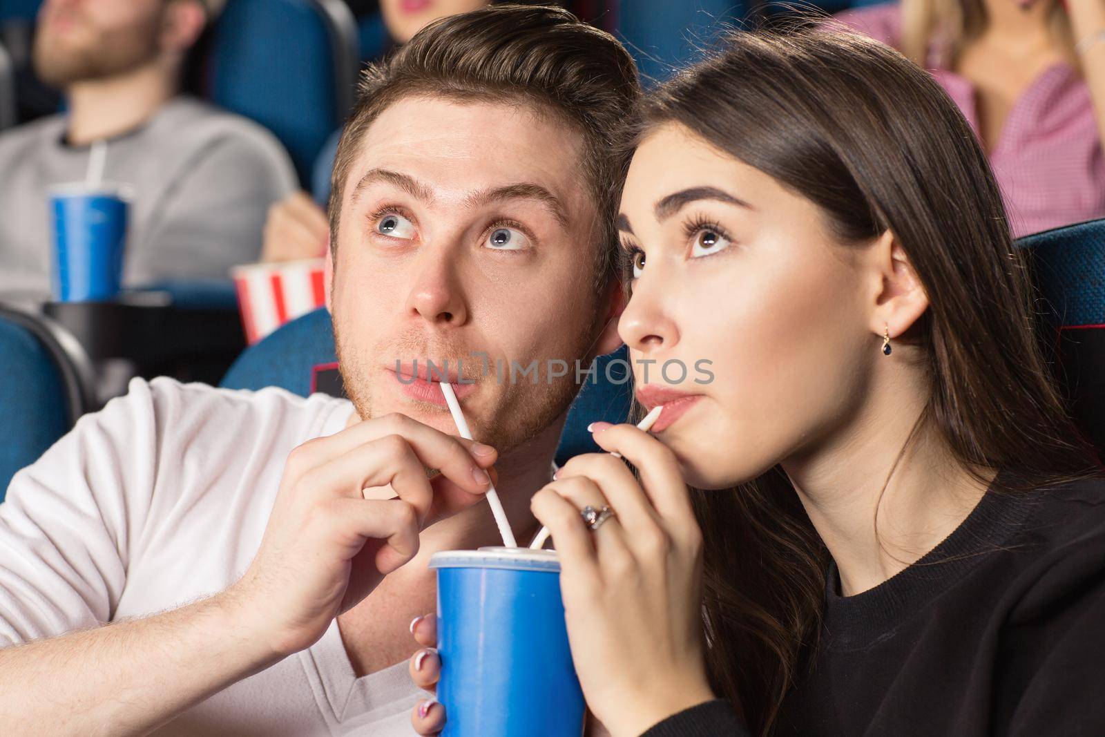 So fascinating. Closeup shot of a young loving drinking the same drink together with two straws in watching movies at the local cinema
