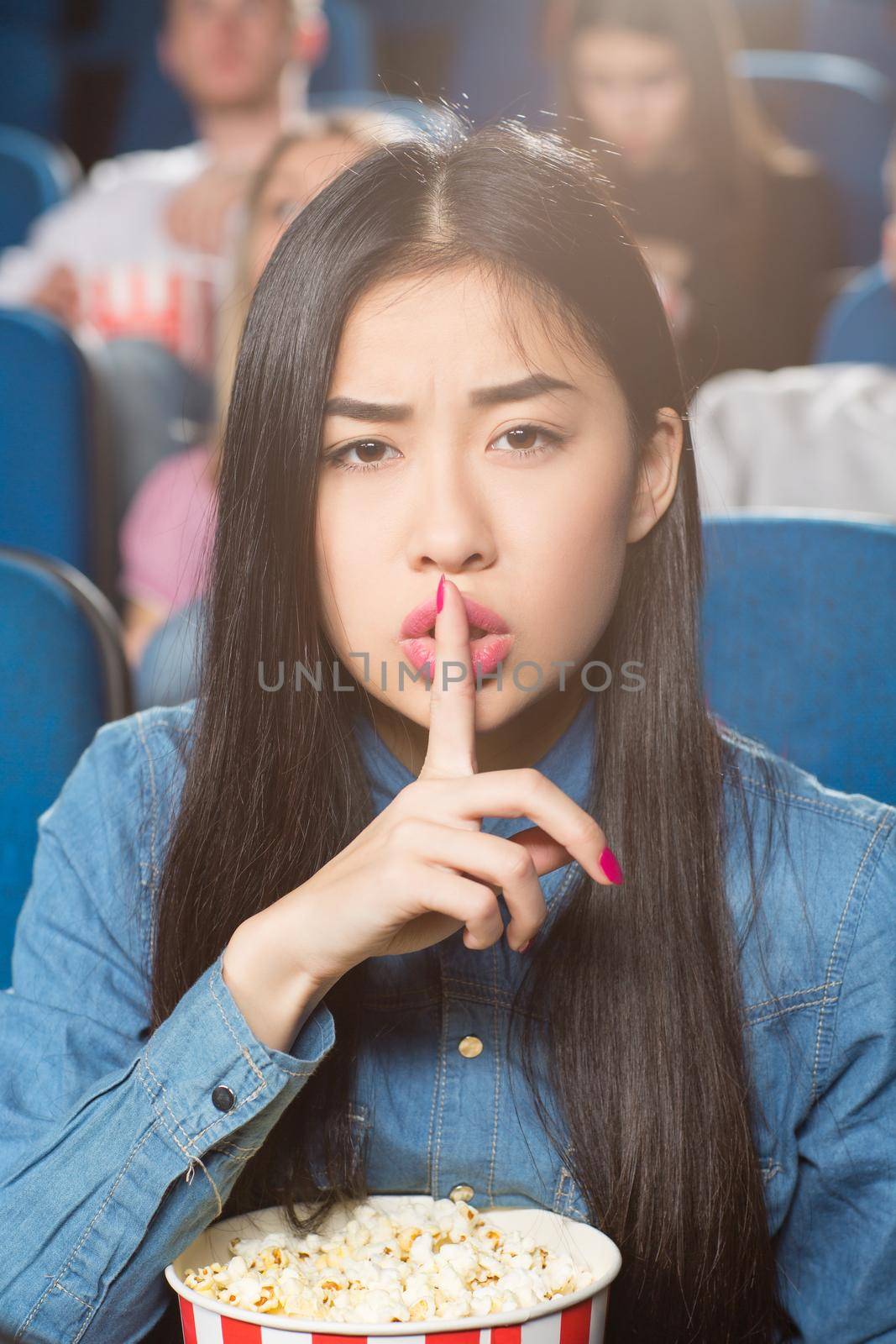 Silence here. Portrait of a beautiful asian woman asking for silence with shushing gesture at the local cinema