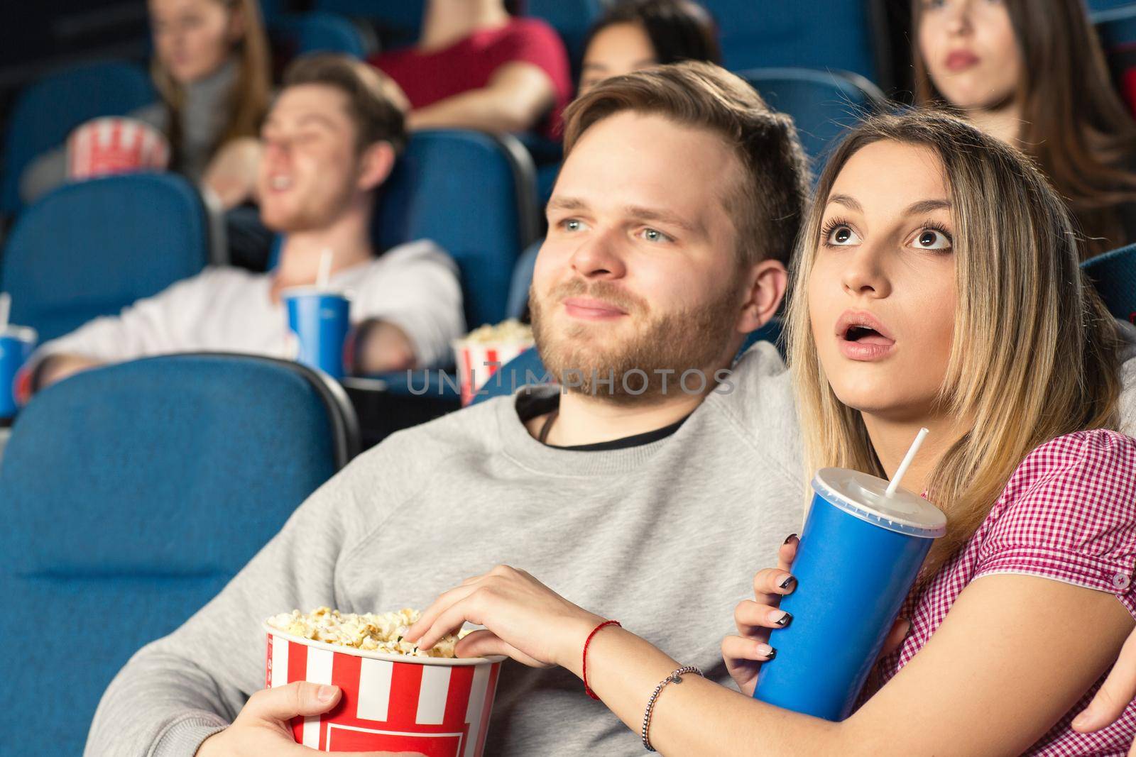 Lady is shocked. Beautiful young couple hugging watching movies together at the cinema