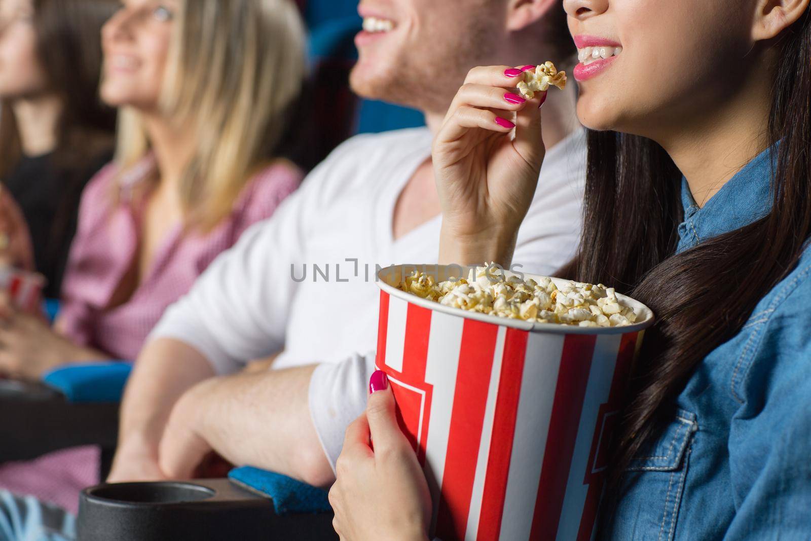 Me and my snack. Cropped closeup of a young woman eating popcorn watching movies with her friends at the cinema