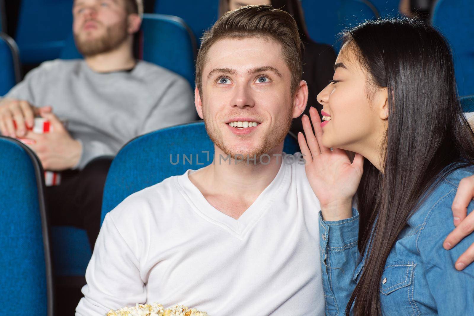 Listen to this. Beautiful young asian woman whispering to her cheerful smiling boyfriend while watching a comedy movie at the cinema