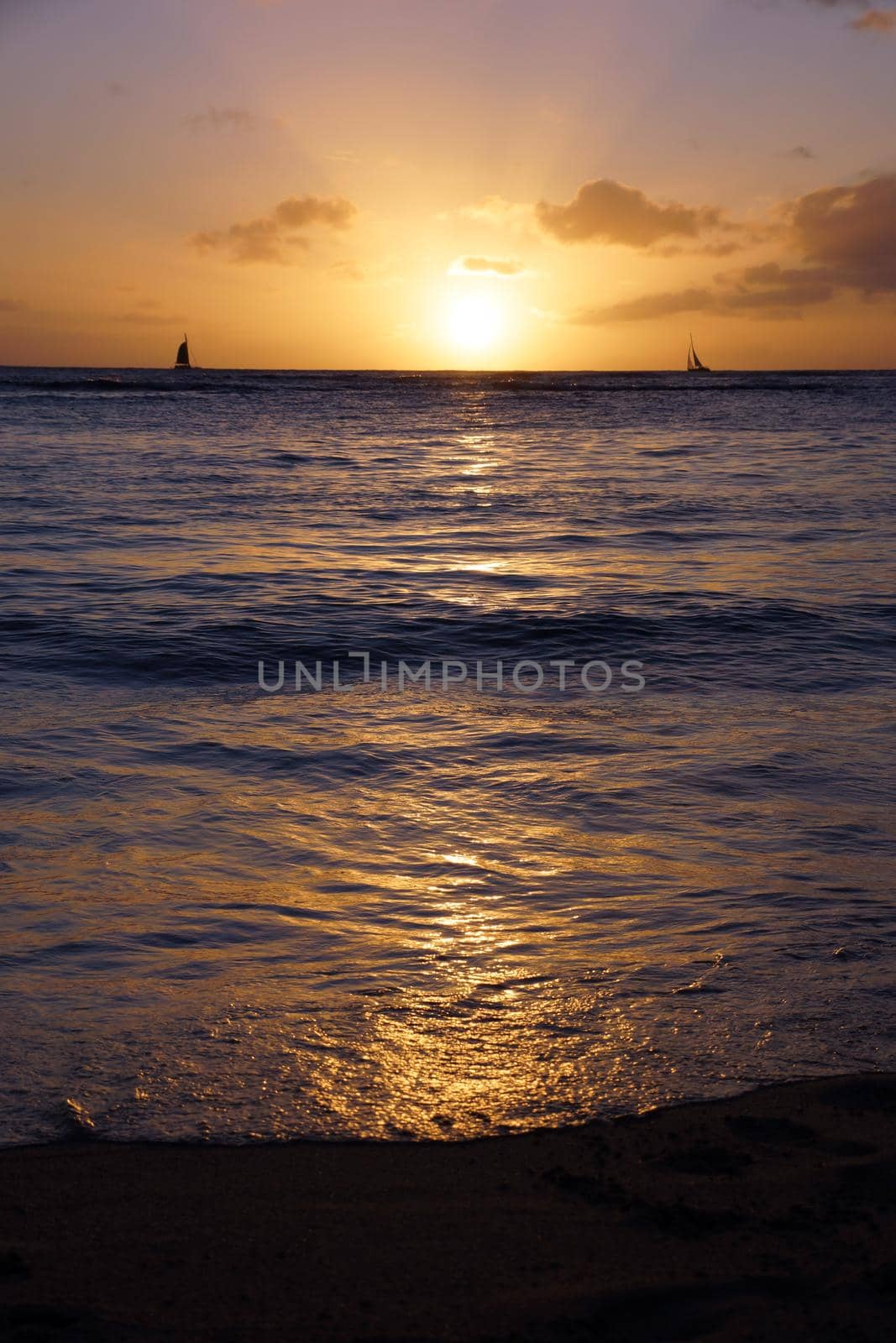 Dramatic Sunset from Waikiki beach over ocean with boats sailing on the water on Oahu, Hawaii.