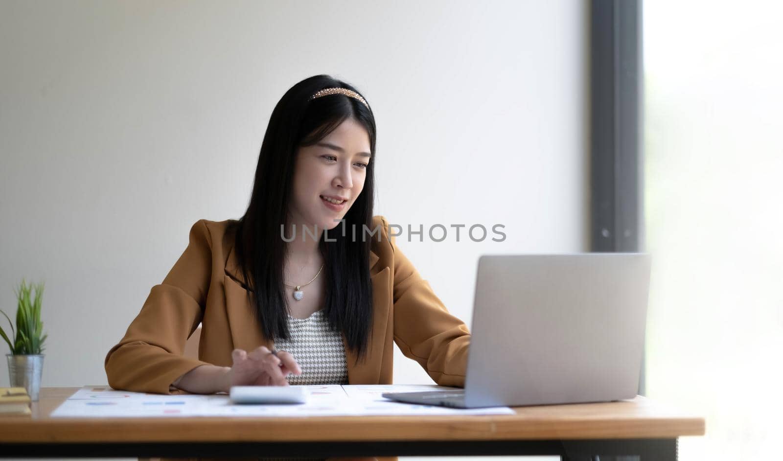 Portrait of asian business woman paying bills online with laptop in office. Beautiful girl with computer and chequebook, happy paying bills. Startup business financial calculate account concept.