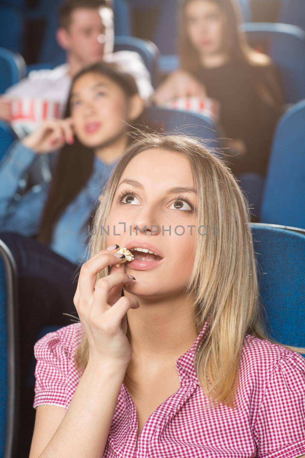 New favorite movie. Vertical shot of a joyful woman eating popcorn watching an interesting movie at the cinema
