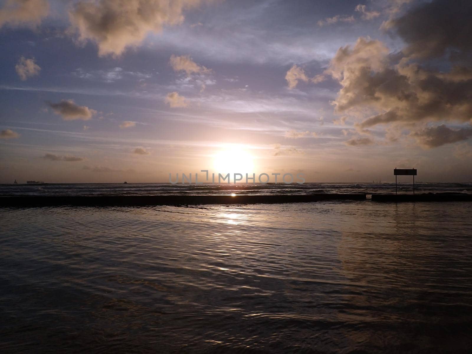 Dramatic Sunset on waters of Waikiki with boats on Horizon and silhouette of sign on Oahu, Hawaii.