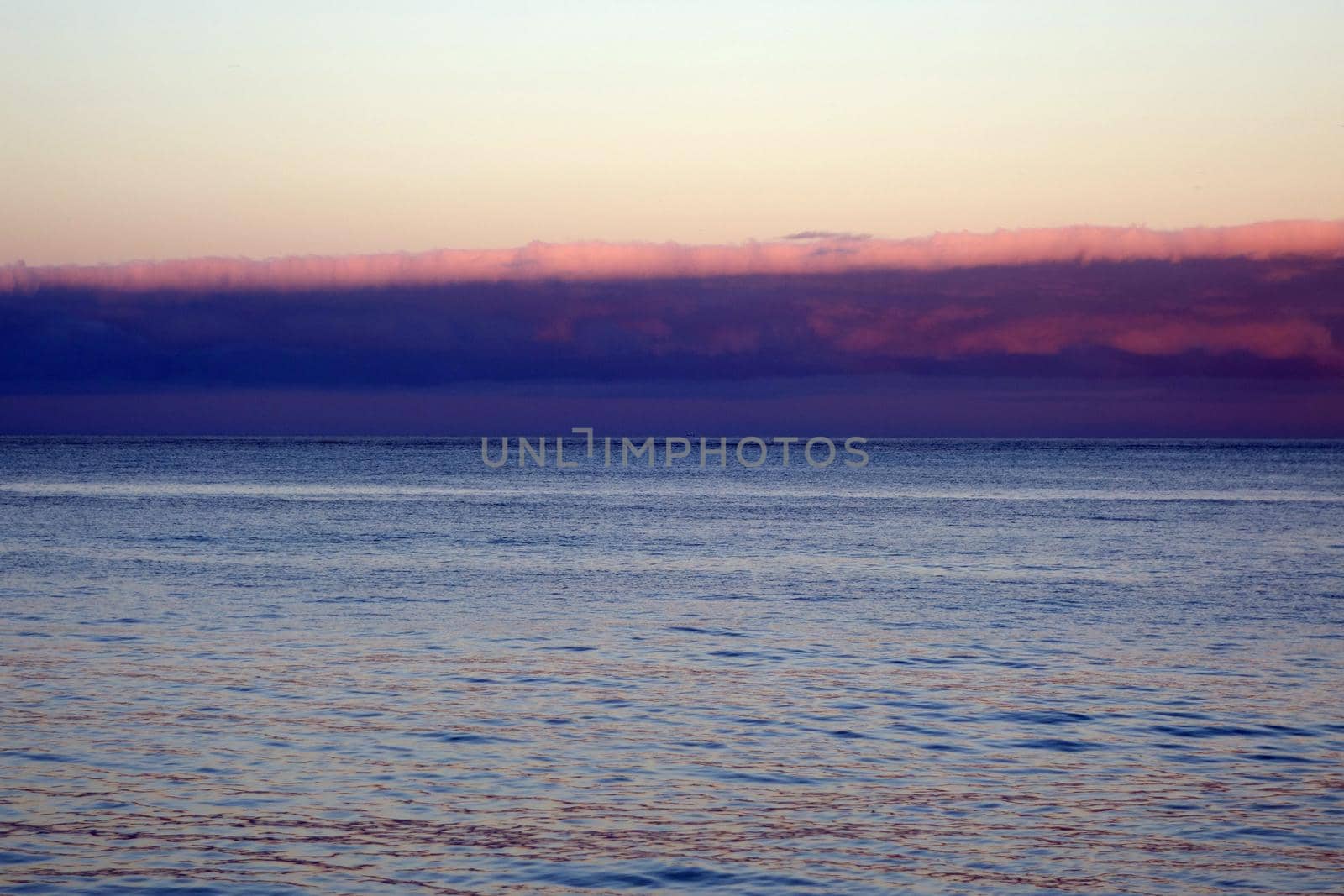 Calm ocean waters of Waimanalo Bay at dusk with clouds hanging overhead on Oahu, Hawaii.                               