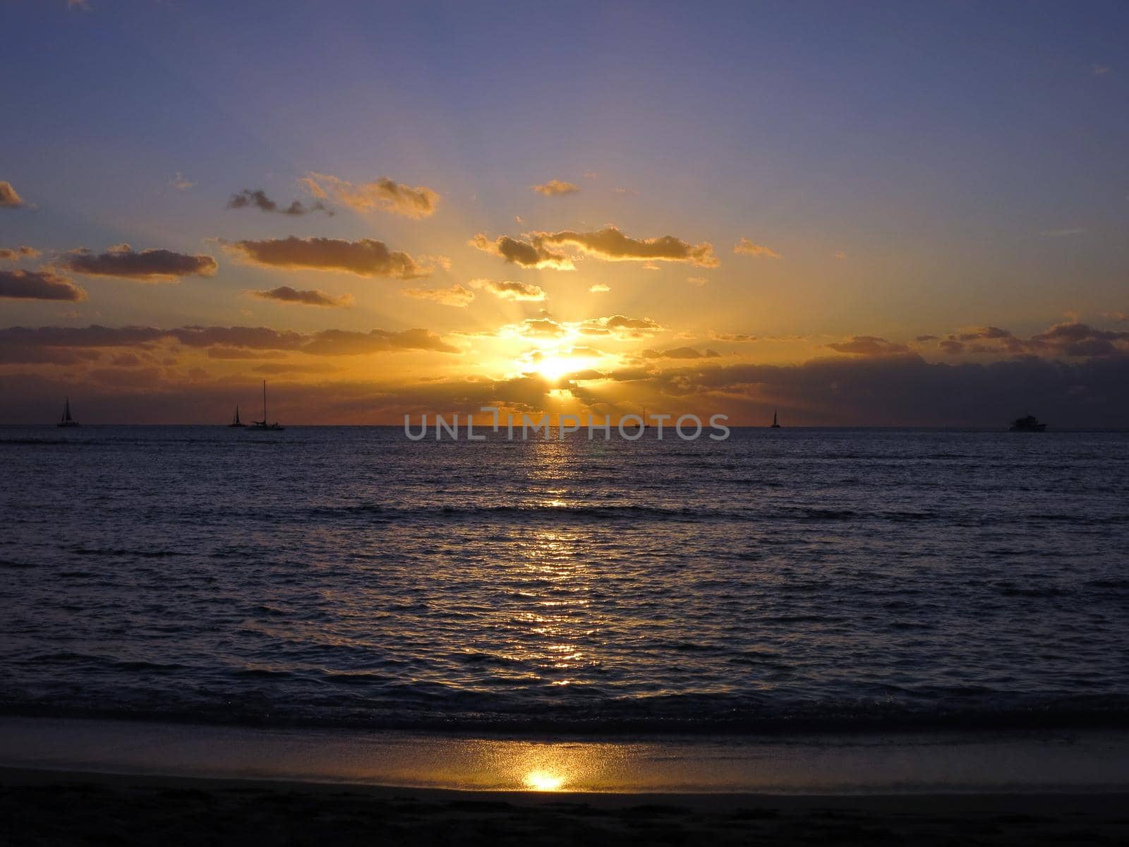 Dramatic Sunset dropping behind the ocean shining over boats on Waikiki Beach on Oahu, Hawaii.