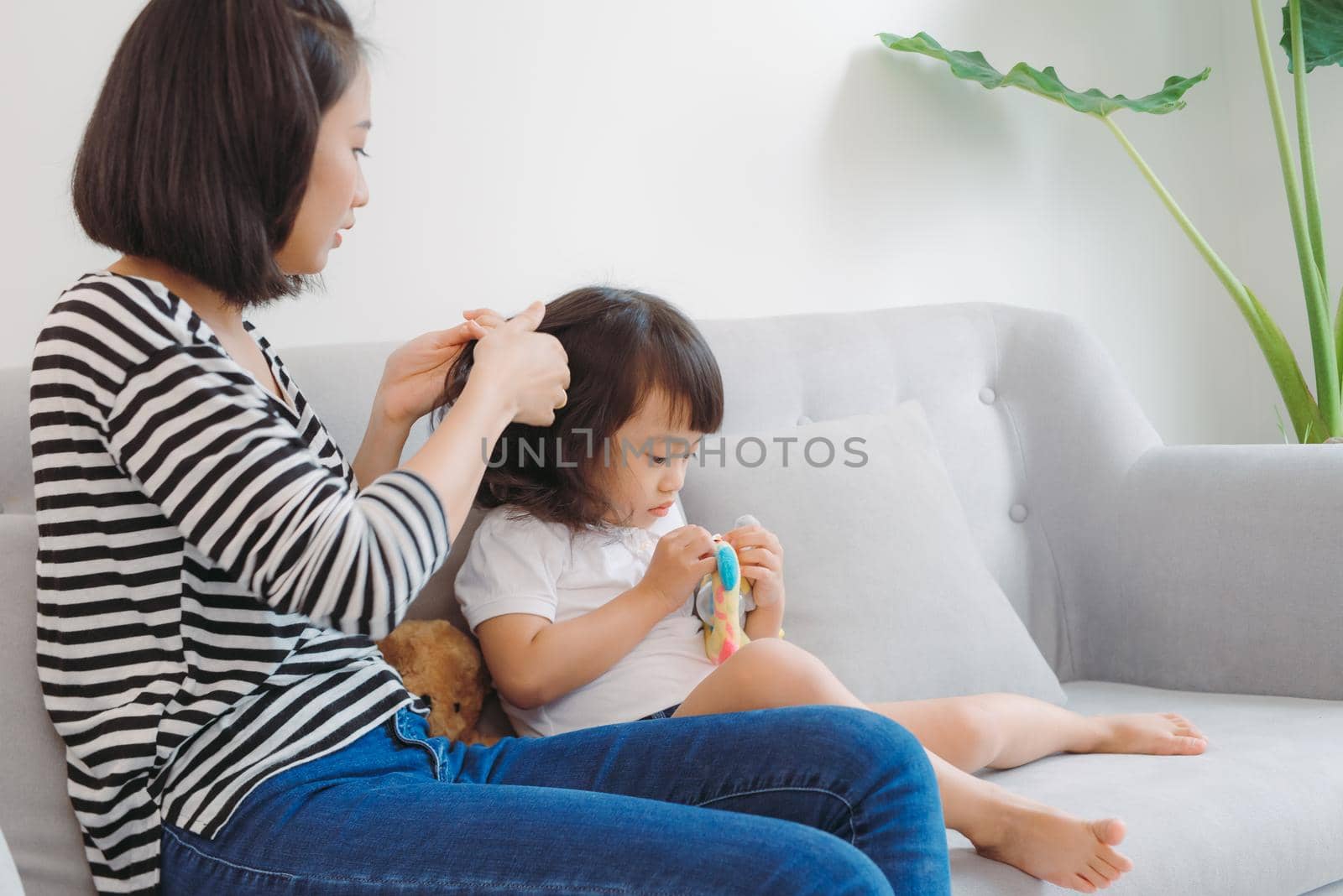 Young loving mother brushing kid daughters hair sitting on sofa,