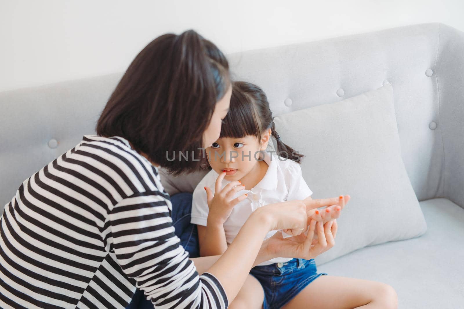 beautiful young mother doing manicure to her cute smiling daughter applying nail polish by makidotvn