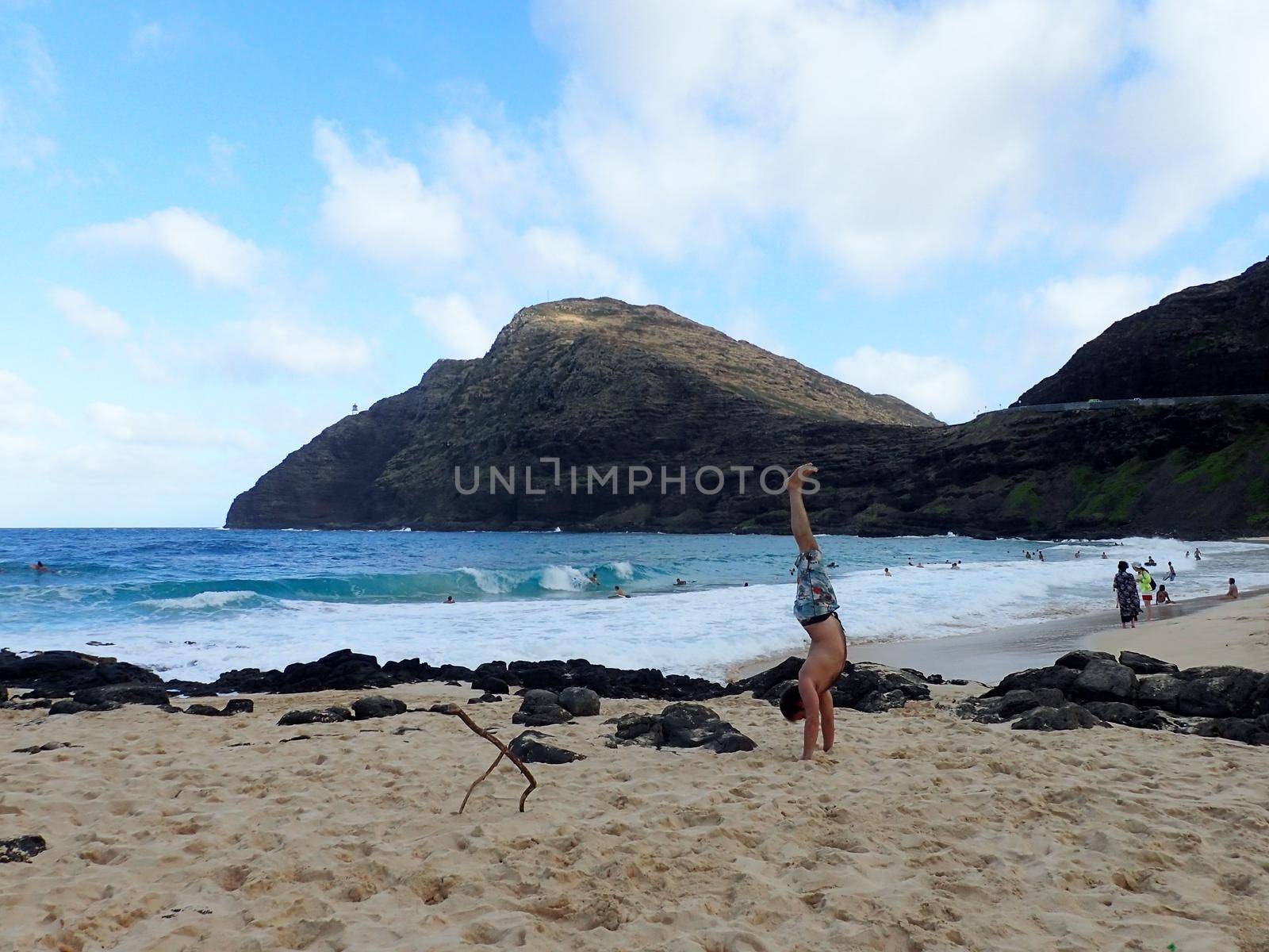 Man Handstanding on Makapuu beach as wave crash on the South east Shore of Oahu, Hawaii.                    