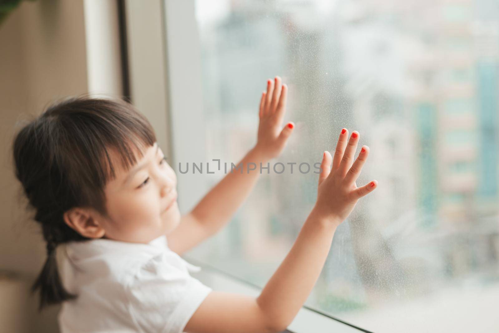 Little asian girl child sitting at home and looking at the window. by makidotvn