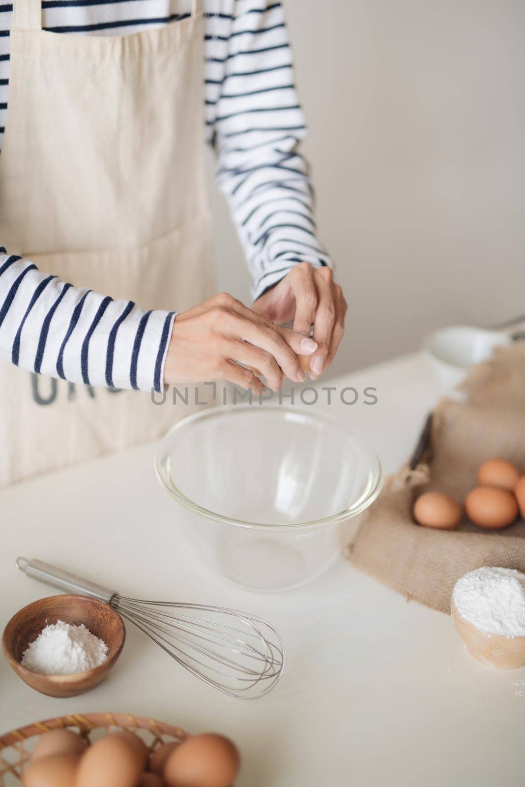Horizontal shot of serious male wearing beige apron breaking egg into metal bowl