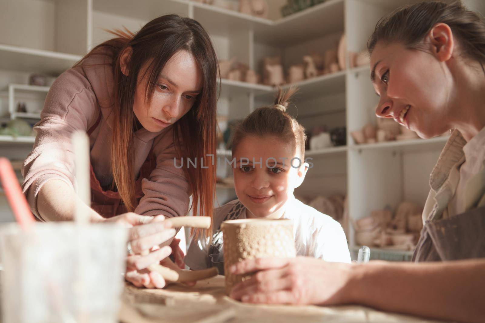 Young boy making ceramic mug with his mother and professional potter