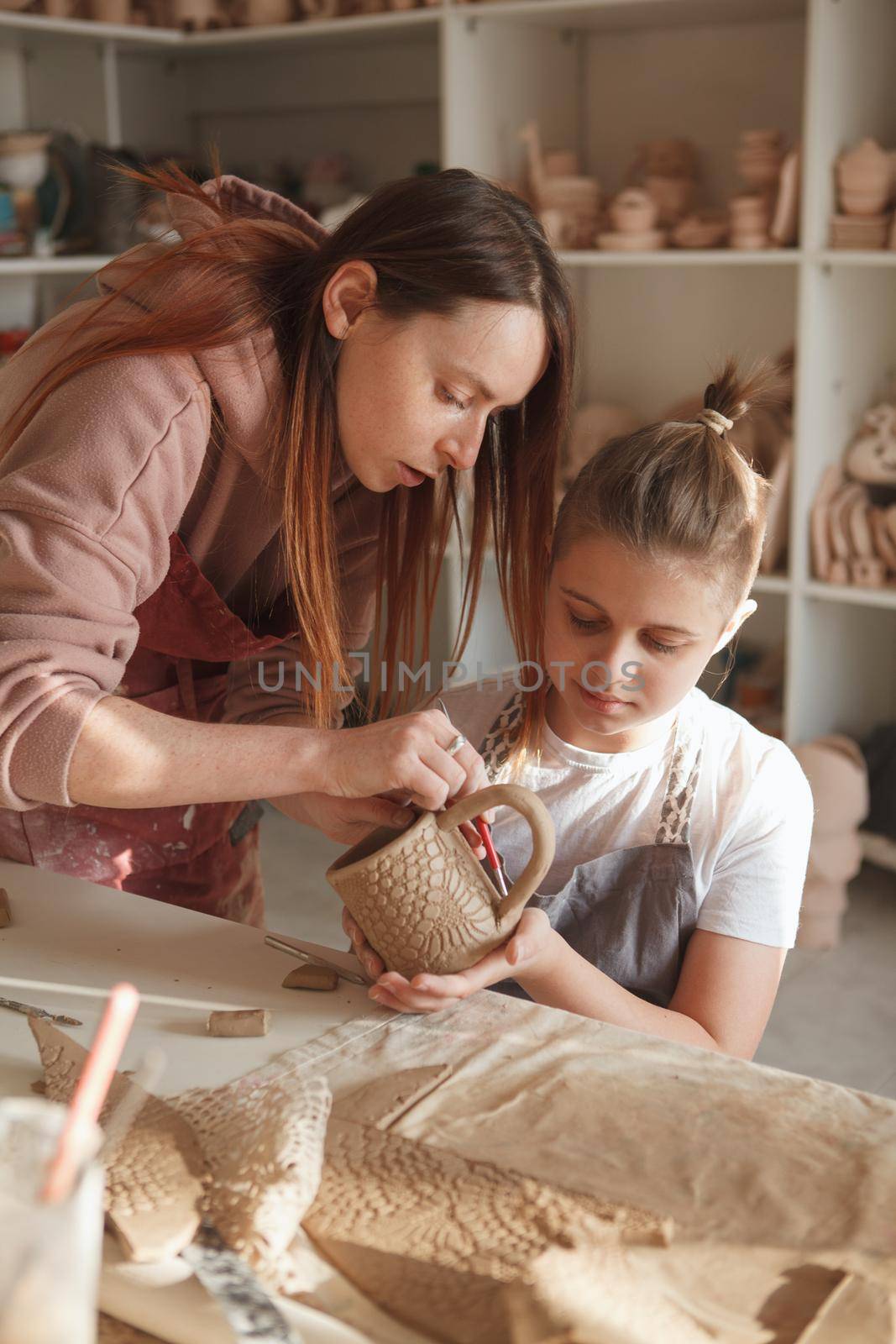 Vertical shot of a female ceramist teaching her young student, making ceramic mug