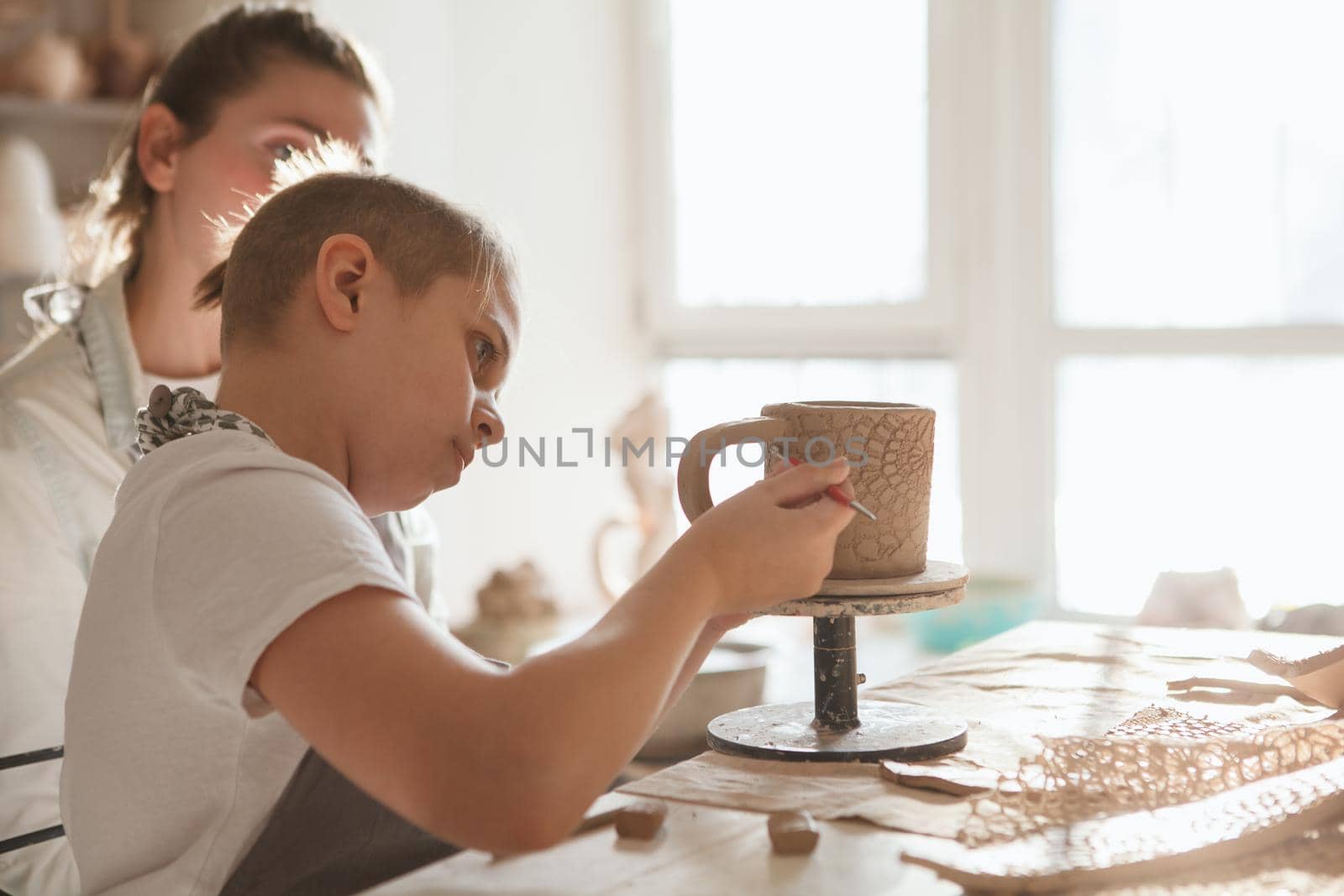 Young boy making ceramic mug with his mother at art class, copy space