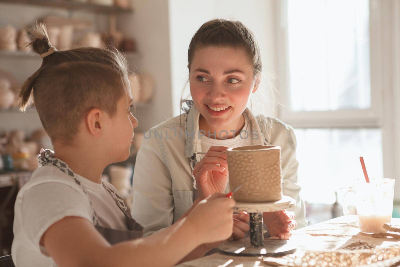 Mother and son smiling at each other while decorating ceramic mug together at art class