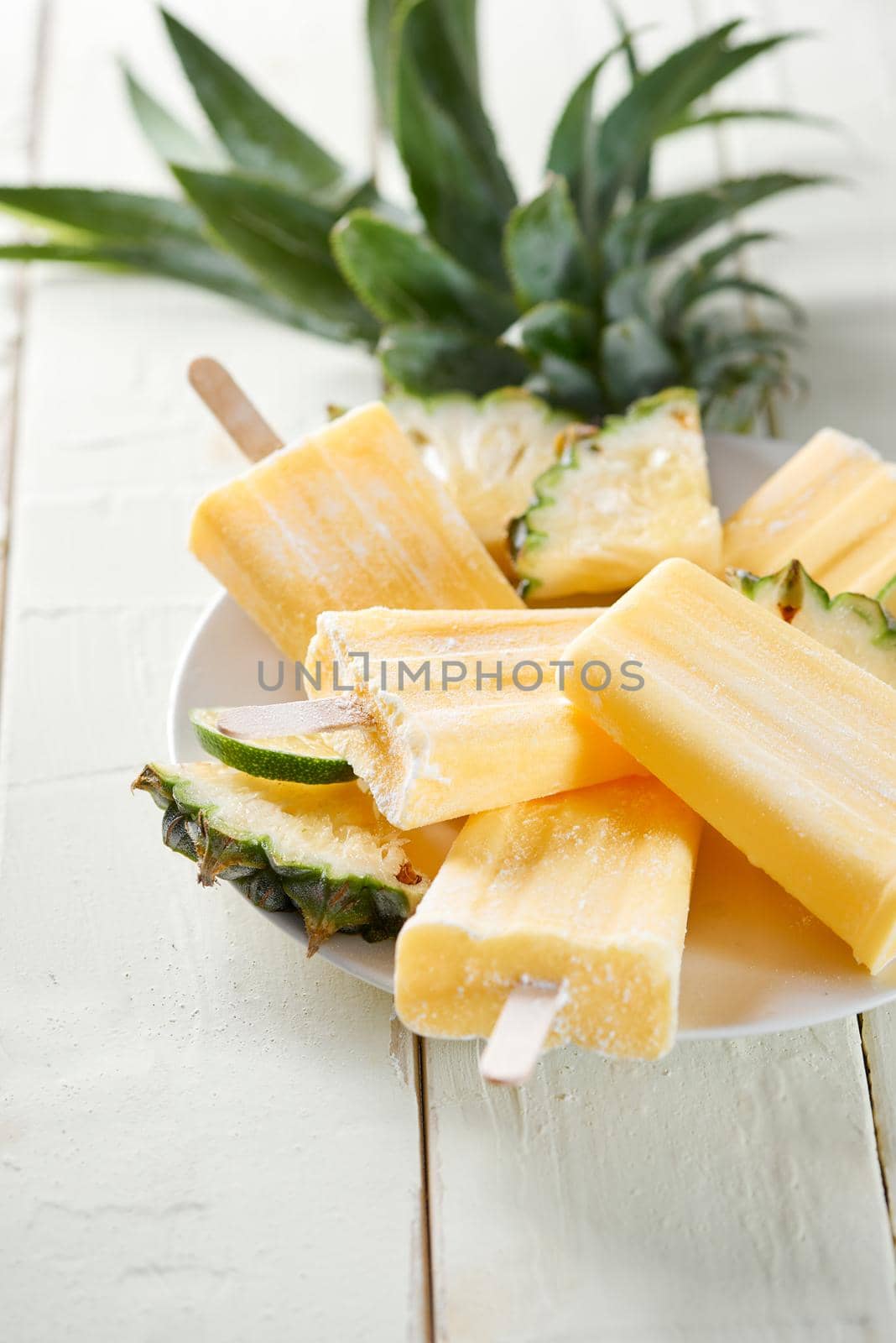 Yellow fruit popsicles on a plate. Top view over a white wood background.