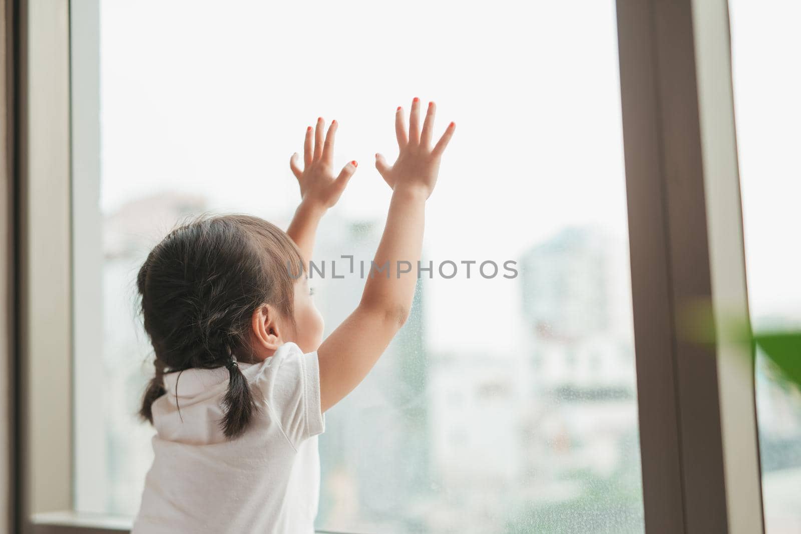 Back view at cute little girl looks out of the window