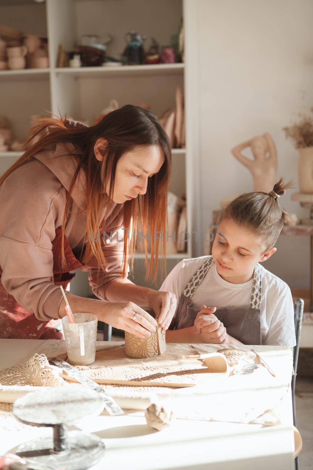Vertical shot of a female ceramist helping her young student during pottery class