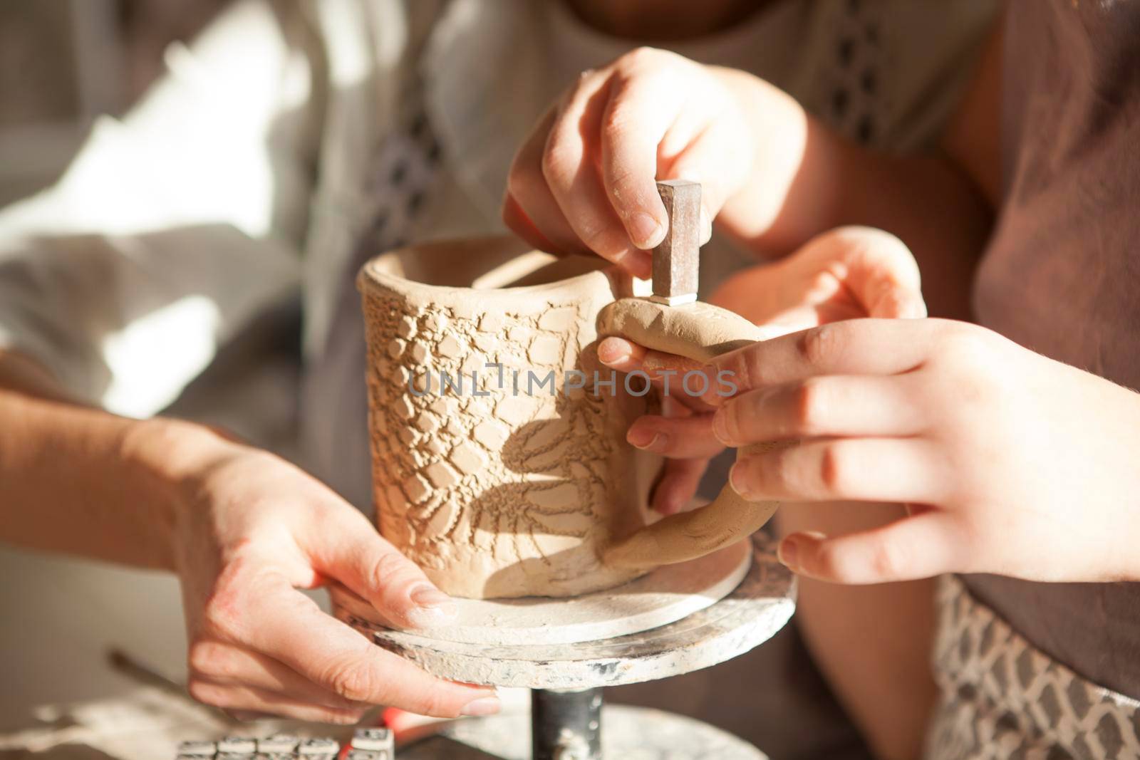 Unrecognizable kid decorating ceramics with stamps, helping mother at pottery class
