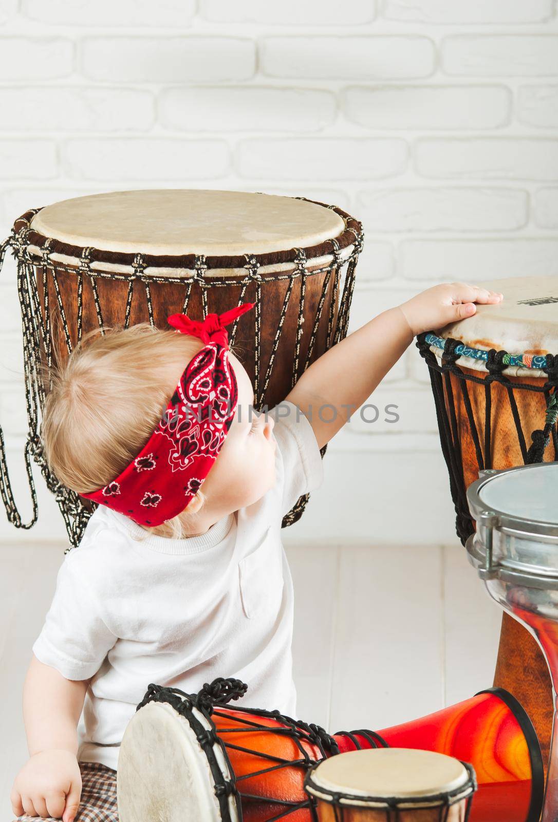 Cute toddler baby playing ethnic drums next to bricks wall