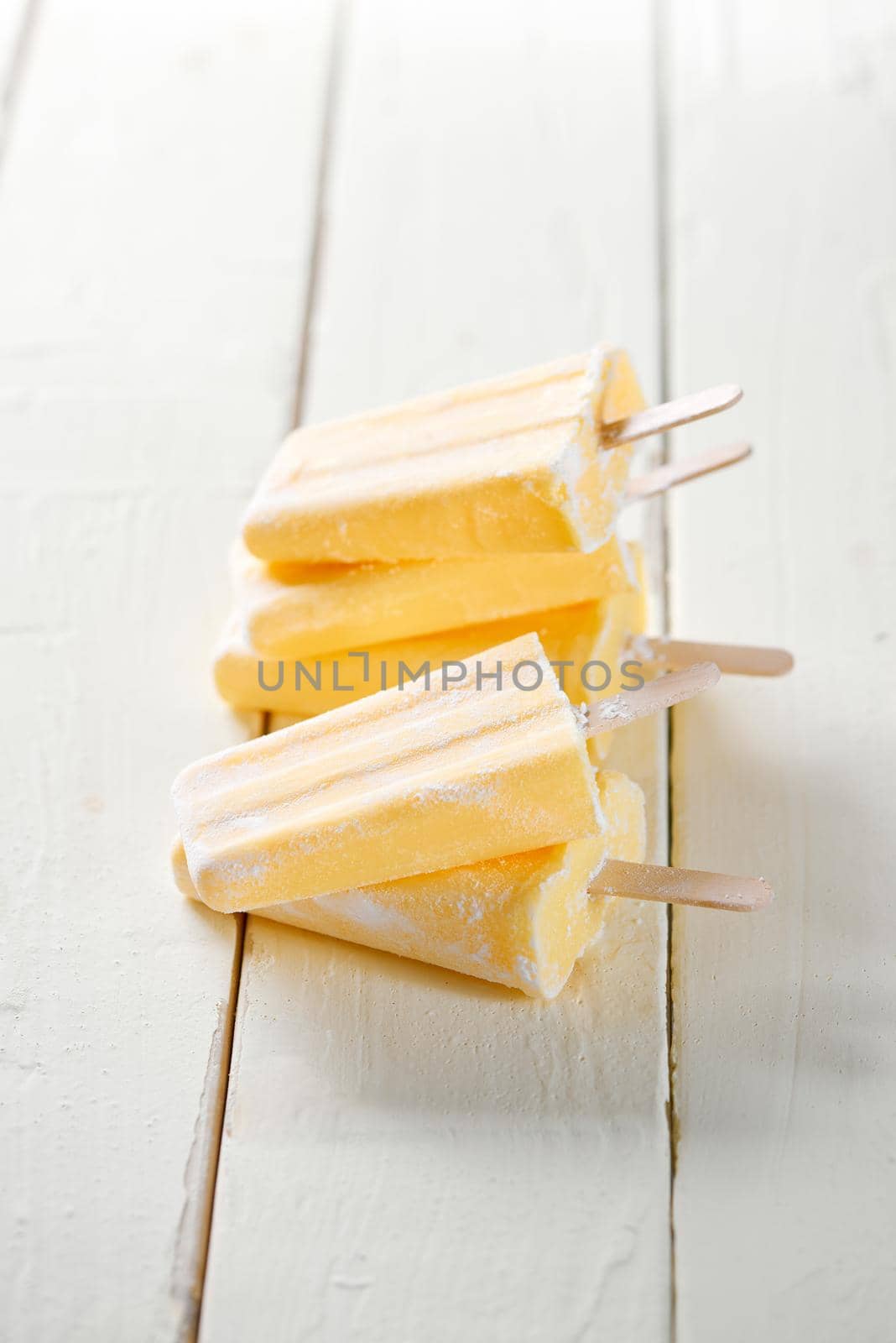 Tall stack of yellow pineapple ice lollies, on a wooden table with white tiled background. Filtered for retro effect