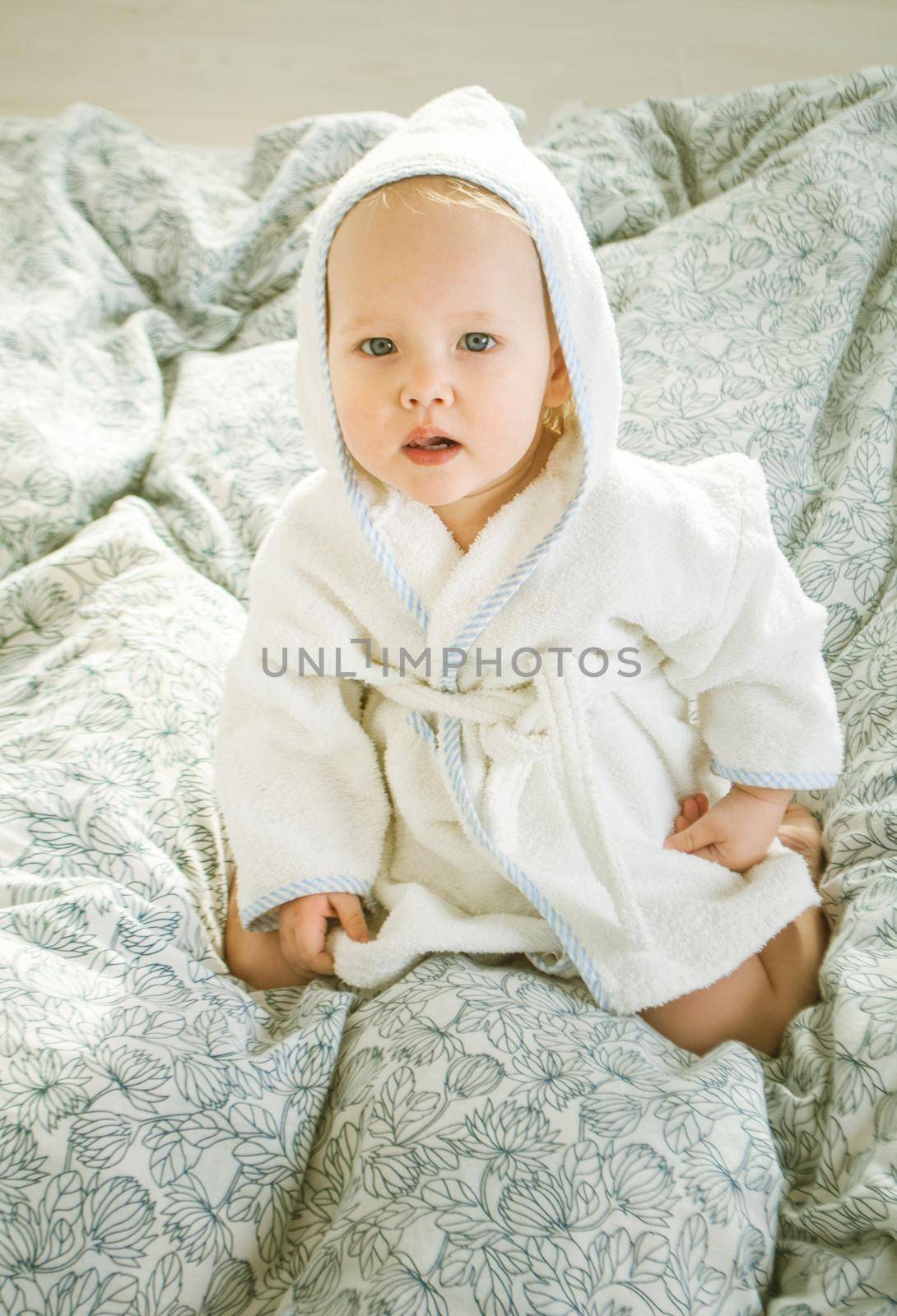 cute babygirl in parents bed in bathrobe and hood on head