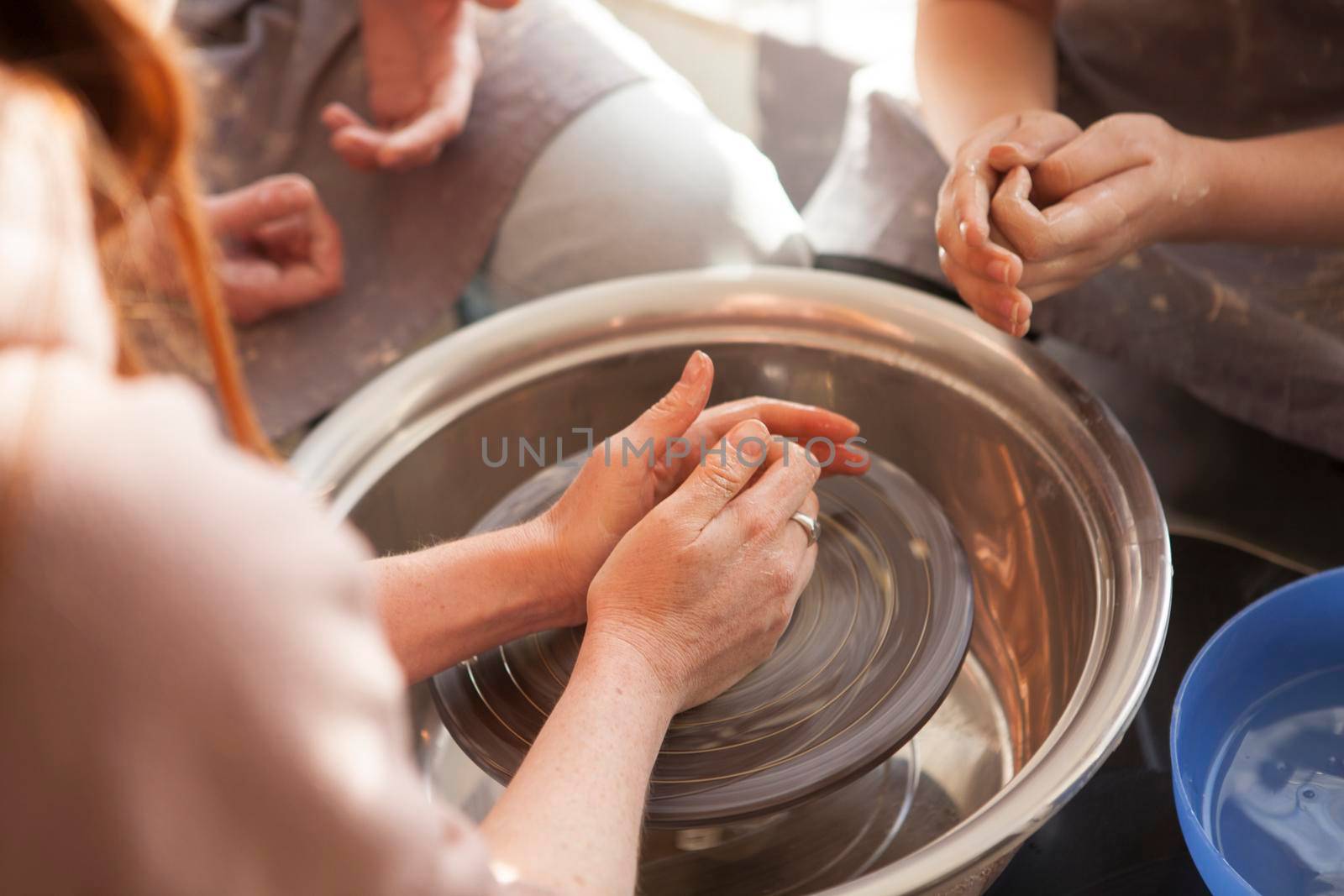Unrecognizable female potter throwing pot on potters wheel, teaching class