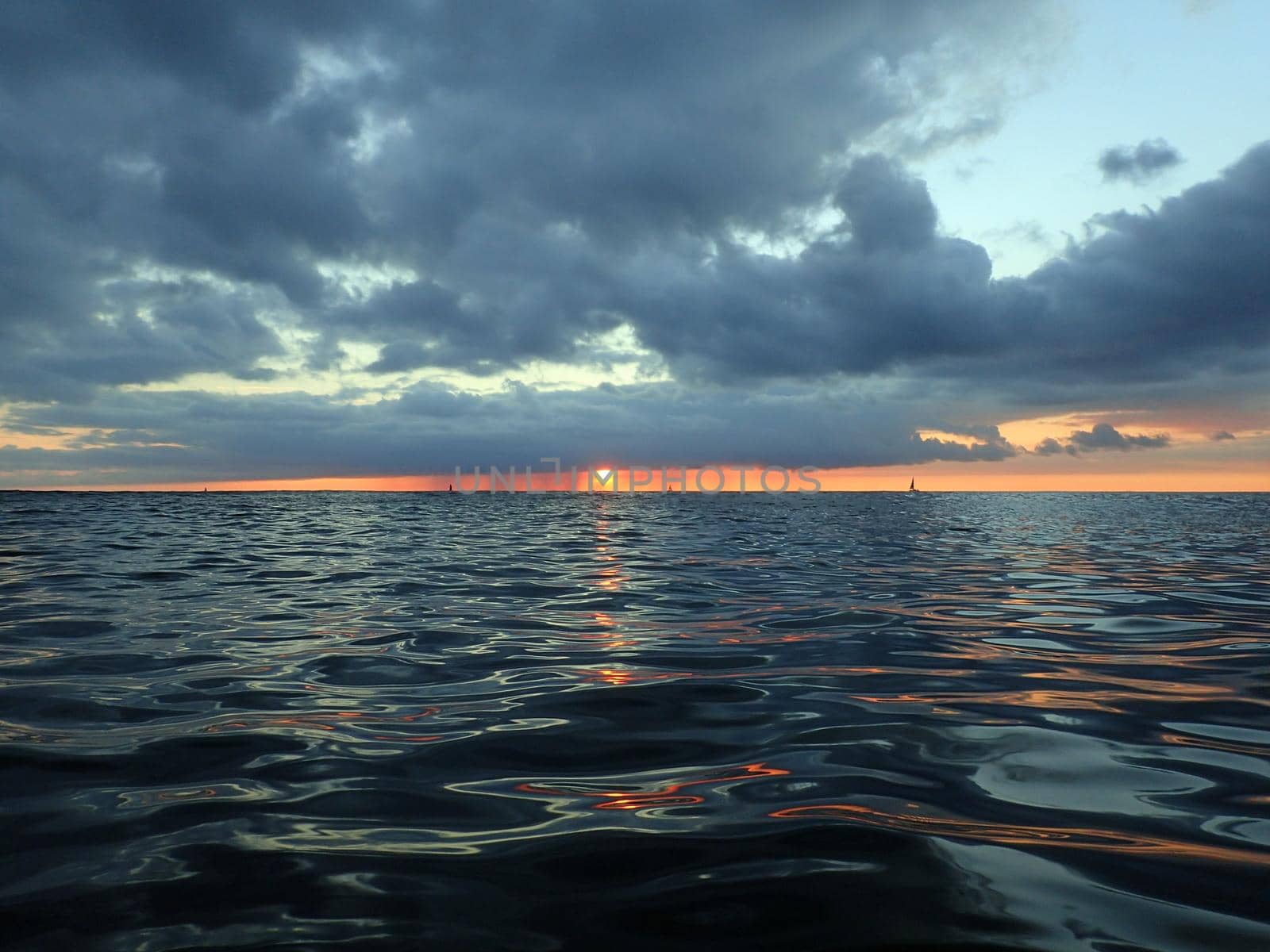 Sun dips below clouds as it lowers to the Pacific ocean with boats on the horizon of the water light reflecting of Oahu, Hawaii.  December 2015.