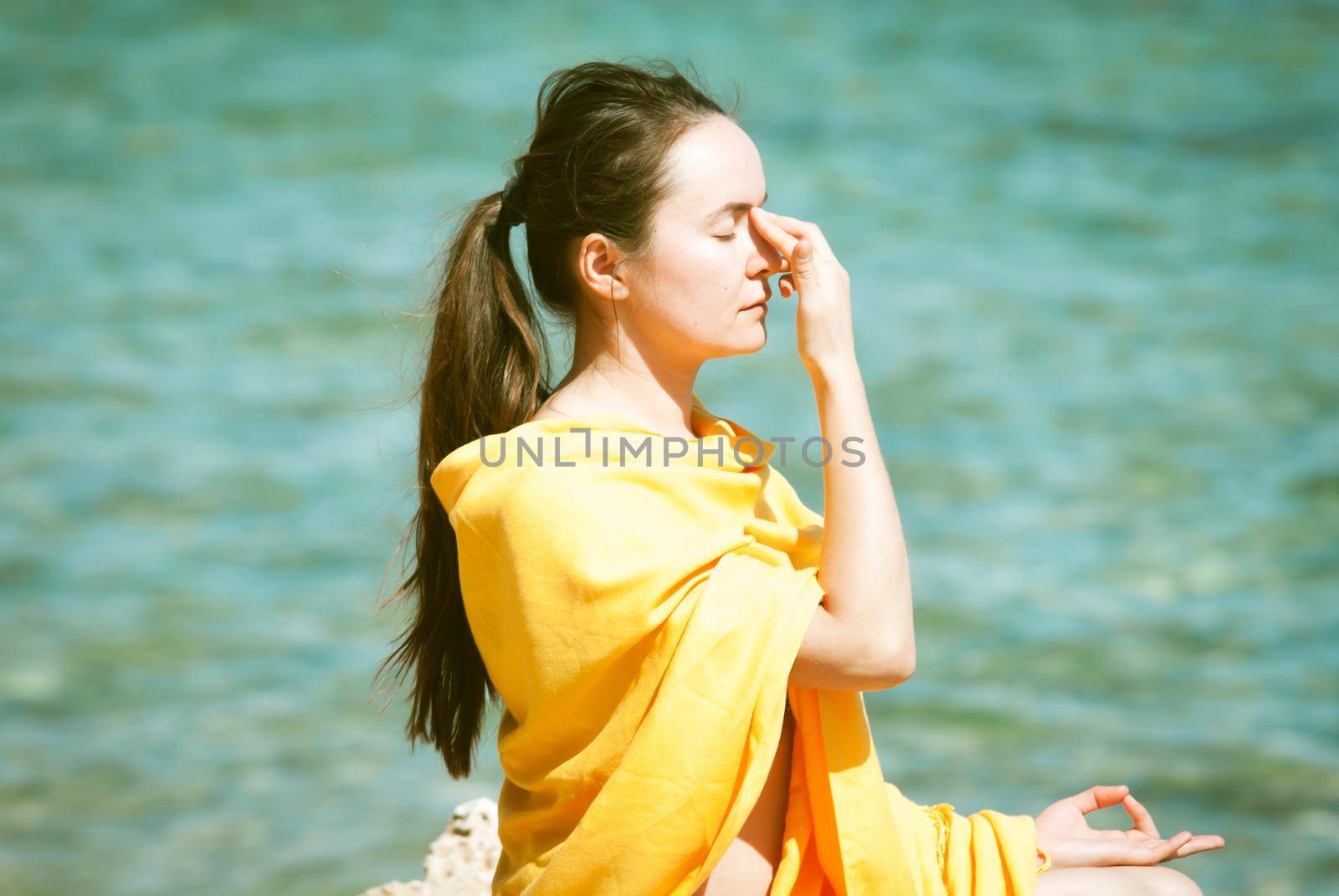 young woman doing yoga breathing pranayama at the blue sea bakcground