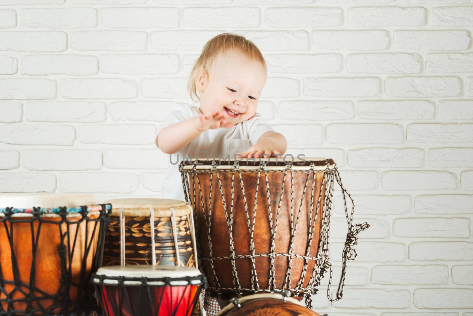 Cute toddler baby playing ethnic drums next to bricks wall
