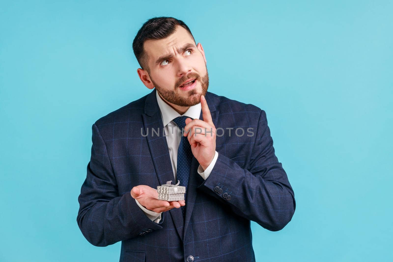 Portrait of pensive man with beard wearing official style suit holding in hands small box with ring, thinking the way to make proposal to his girlfriend. by Khosro1