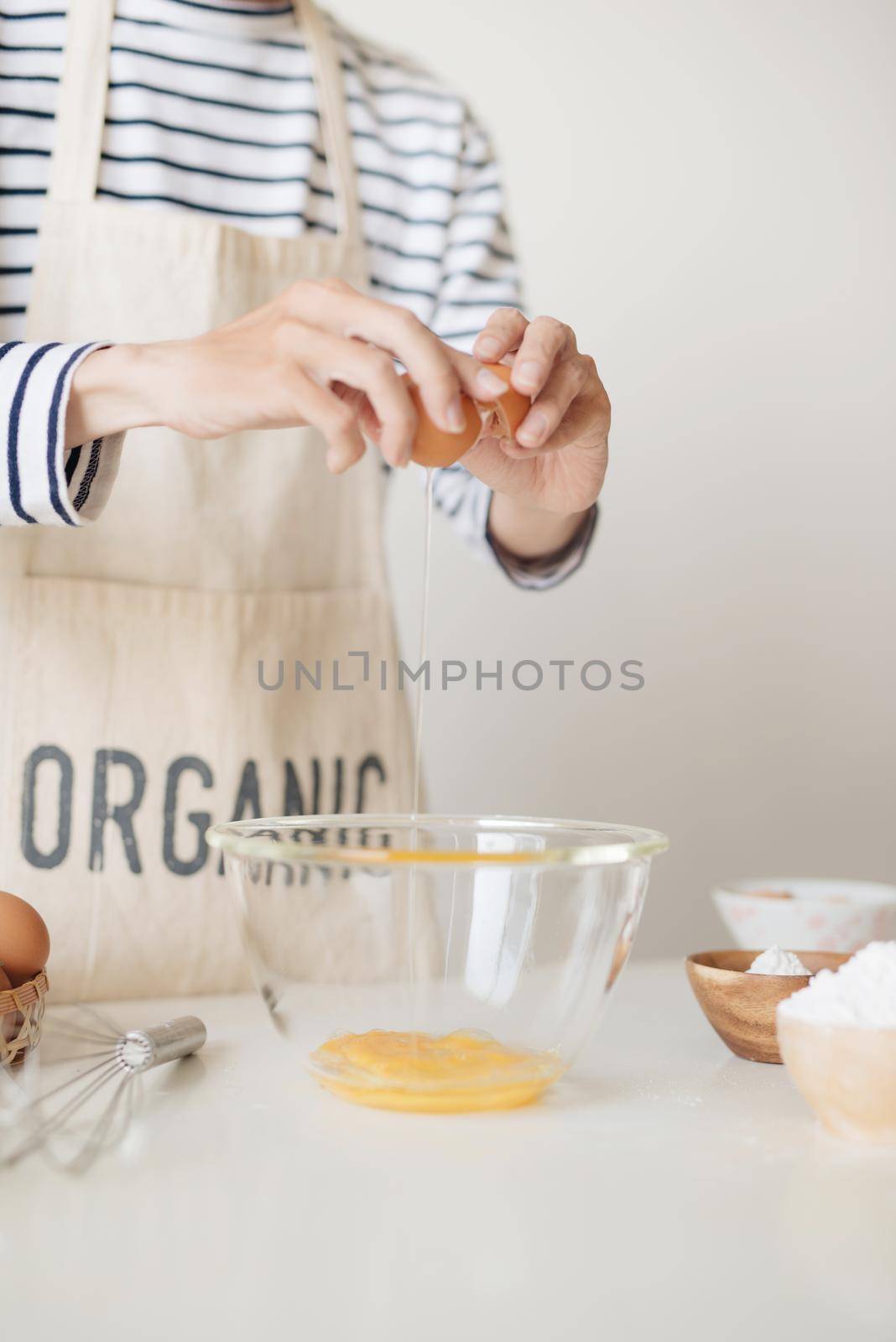 Horizontal shot of serious male wearing beige apron breaking egg into metal bowl by makidotvn