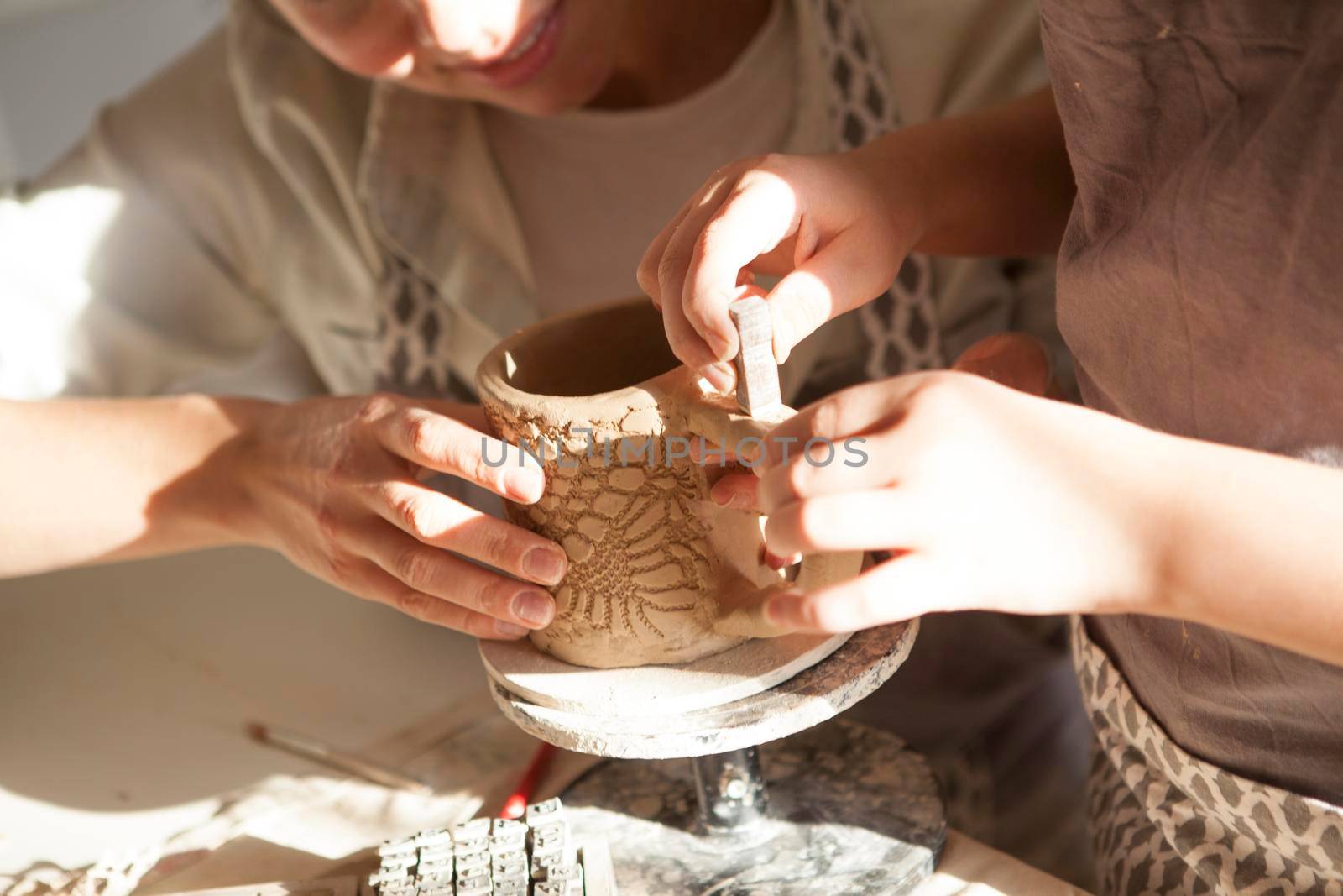 Cropped close up of a child and mother decorating ceramic mug with stamps