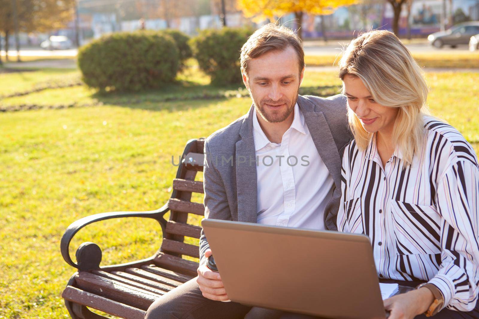 Mature businessman discussing project with his female colleague outdoors in the park. Technology, internet concept