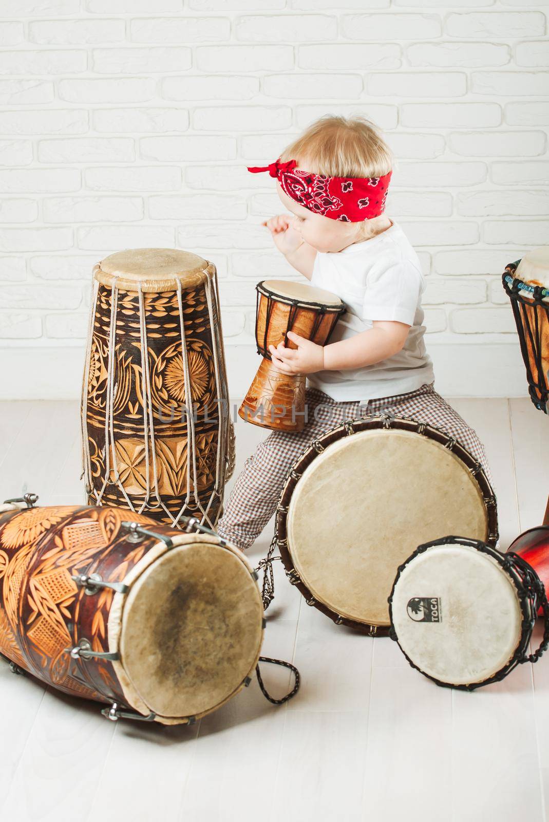 Cute toddler baby playing ethnic drums next to bricks wall