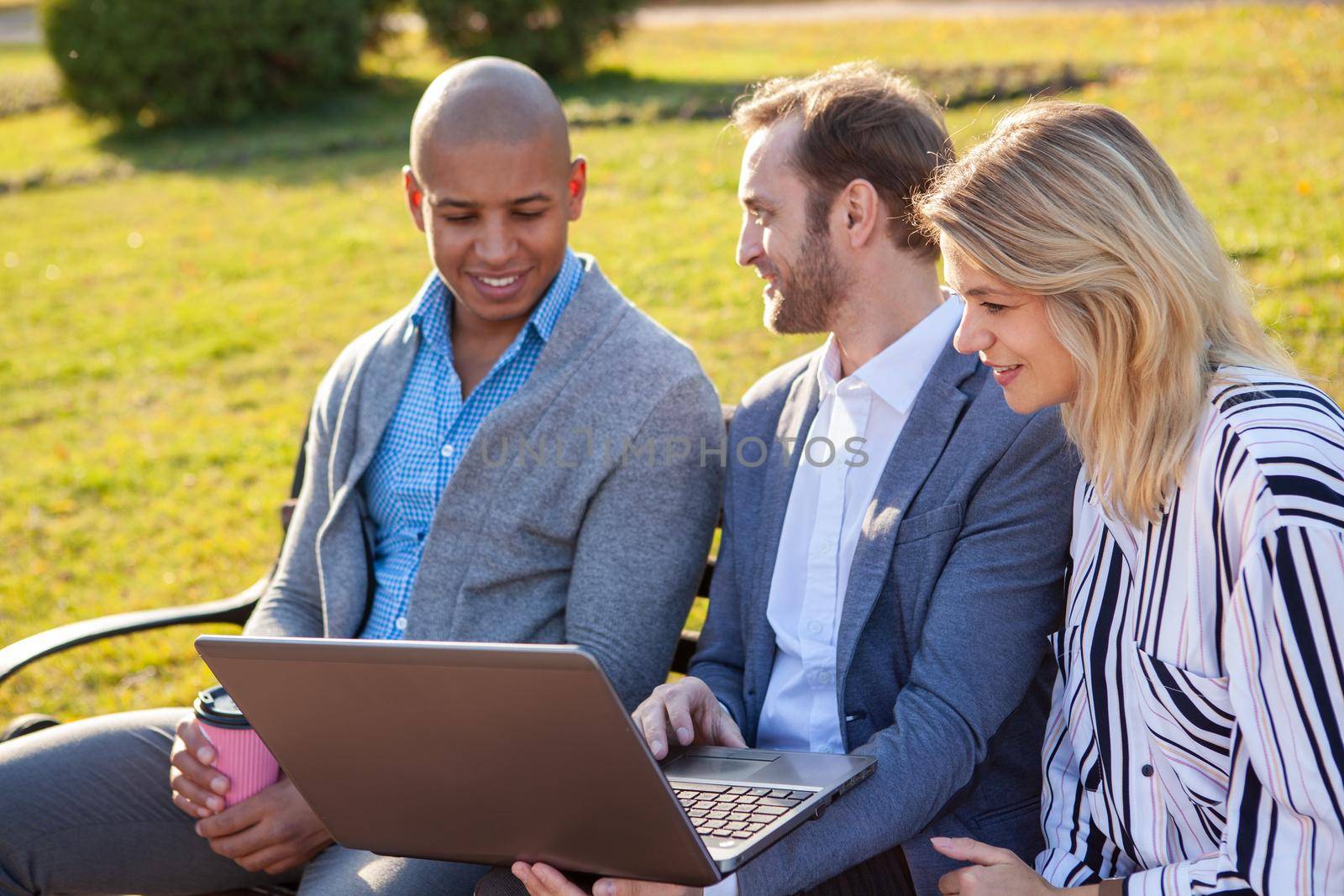 Mature businesswoman meeting with her male colleagues outdoors in the park. Business team discussing project, using laptop