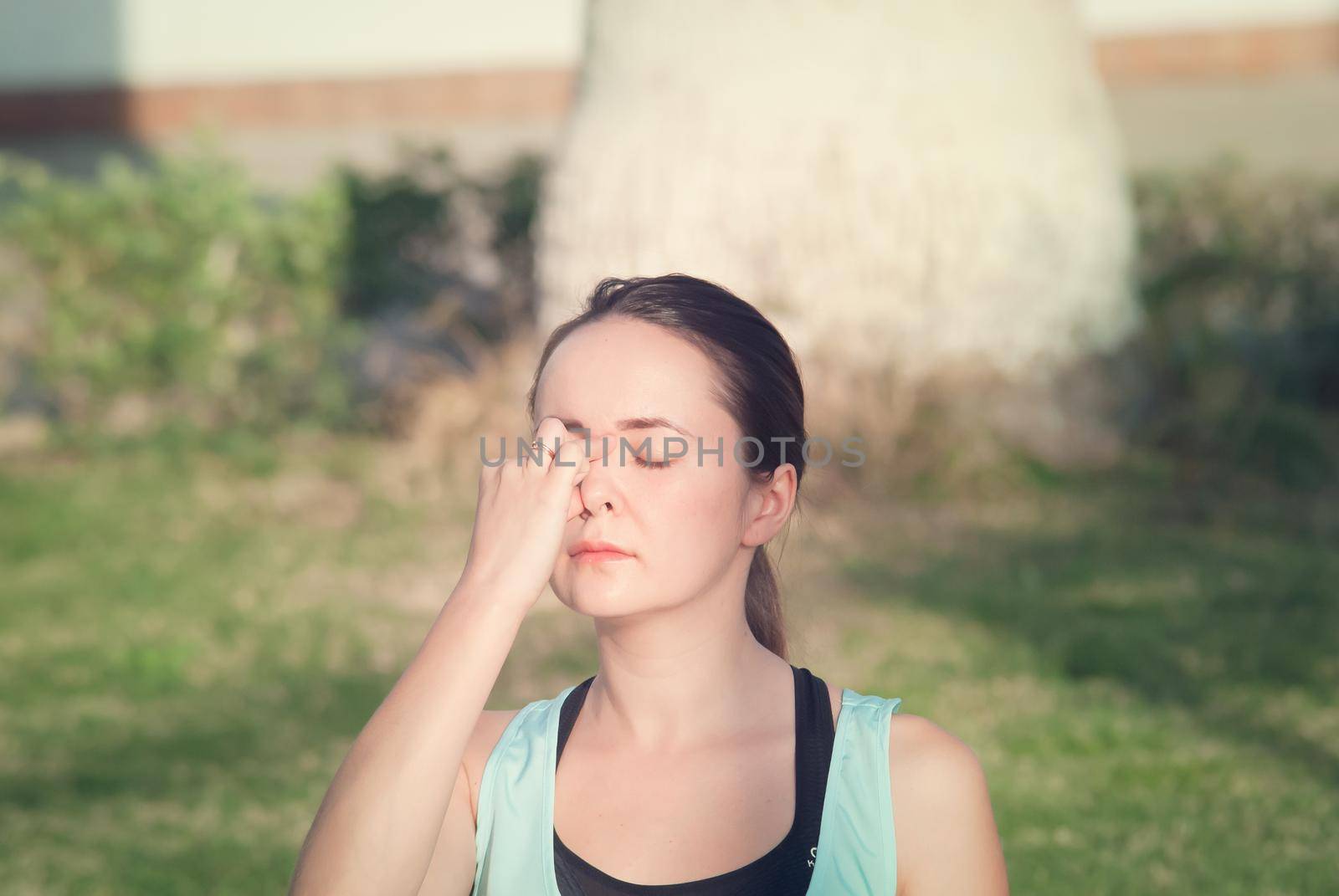 Young woman doing breathing yoga at green grass in the park in the morning